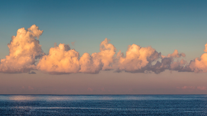 Wolken boven zee met lichte gloed in roze en oranje